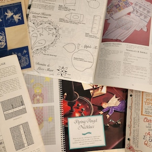 May include: A collection of craft and embroidery patterns, including a heart-shaped pattern, a denim and lace shirt pattern, a flying angel necklace pattern, and a pattern for sponged squares. The patterns are printed on paper and include instructions for creating the projects.