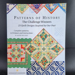 May include: A book titled "Patterns of History: The Challenge Winners" featuring 23 quilt designs. The cover displays colorful quilt patterns with text that reads "Complete patterns, techniques and instructions by Kathy Delaney."