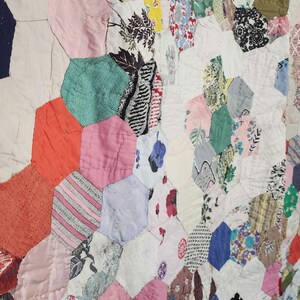 May include: A patchwork quilt made of various fabrics in shades of pink, red, blue, green, and white. The quilt is made up of hexagonal shapes, each with a different pattern. The quilt is a traditional style and is likely handmade.