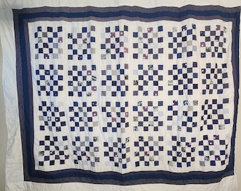 May include: A white quilt with a checkerboard pattern in shades of blue and purple. The quilt is edged with a dark blue border and a white border with small blue dots.
