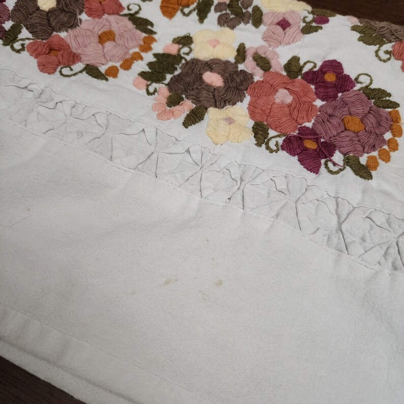 Puede incluir: Tela blanca con bordado floral colorido. El bordado presenta flores en tonos rosa, naranja, marr&oacute;n y morado, con hojas verdes. Una cenefa decorativa est&aacute; cosida debajo del dise&ntilde;o floral.