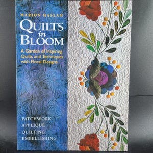 May include: A book cover titled "QUILTS in BLOOM" by Marion Haslam. The cover features a blue and white background with floral designs. The text reads "A Garden of Inspiring Quilts and Techniques with Floral Designs". Keywords: Patchwork, Appliqué, Quilting, Embellishing.