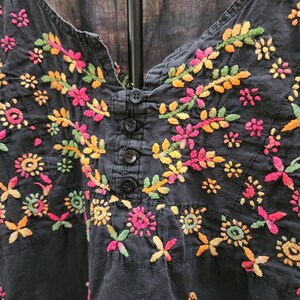 Peut inclure: Haut noir brod&eacute; avec un d&eacute;collet&eacute; en V et une fermeture boutonn&eacute;e. Le haut pr&eacute;sente des broderies florales color&eacute;es dans les tons de rose, jaune, orange et vert. La broderie est d&eacute;taill&eacute;e et couvre le devant du haut.