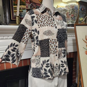 May include: A button-down shirt with a patchwork design featuring leopard print, leaf patterns, and geometric shapes in black, beige, and brown. The shirt has long sleeves and a collared neckline.