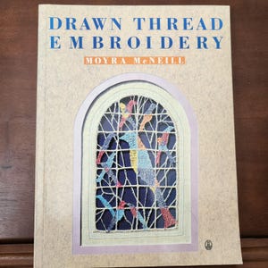 May include: A book titled "Drawn Thread Embroidery" by Moyra McNeill. The cover features a colorful embroidered design of birds and branches in a window frame.