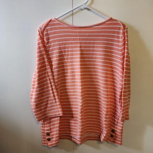 May include: A coral and white striped long-sleeved shirt with button details on the cuffs.