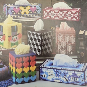 Puede incluir: Una colección de seis fundas para cajas de pañuelos rectangulares y cuadradas hechas de malla plástica con varios diseños de punto de aguja, incluyendo un payaso, un patrón de corazones arcoíris, una escena de sauce azul y motivos geométricos.