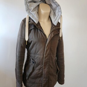 May include: A brown hooded jacket with a zipper closure and a white drawstring. The jacket has a quilted design and multiple pockets.