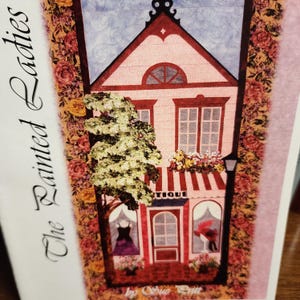 May include: A colorful illustration of a boutique shop with a red and white striped awning, a tree, and flower boxes. The text "The Painted Ladies" is on the left side of the image. The shop has a red door and windows.