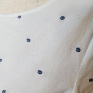 May include: White fabric with a subtle pattern of small, dark blue polka dots.
