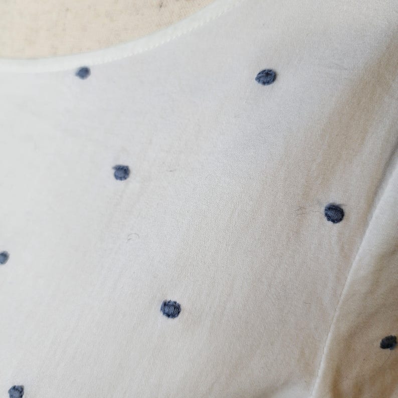 May include: White fabric with a subtle pattern of small, dark blue polka dots.