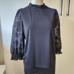 May include: A black mock neck top with sheer floral patterned sleeves. The sleeves have a ruffled edge.