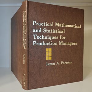 May include: A brown hardcover book titled Practical Mathematical and Statistical Techniques for Production Managers by James A. Parsons. The cover features gold text and a small yellow grid icon. The spine also displays the title and author.
