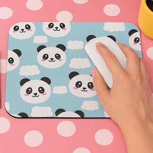 May include: A rectangular mouse mat with a light blue background featuring a pattern of cartoon panda faces and white clouds. A white computer mouse rests on the mat. A keyboard and a yellow pot with a plant are also visible.