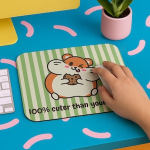 May include: A rectangular mousepad with a green and white striped background. The mousepad features a cartoon hamster holding a cookie, with the text "100% cuter than you".