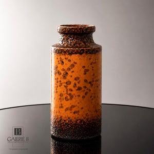 Könnte beinhalten: Eine zylindrische Keramikvase mit einem texturierten dunkelbraunen Rand und Boden sowie einem glatten, leuchtend orangefarbenen Mittelteil, der mit dunkelbraunen Sprenkeln verziert ist. Die Vase hat einen schmalen Hals und eine breite Öffnung.