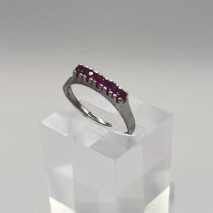Könnte beinhalten: Ein silberner Ring mit einer Reihe von fünf roten Edelsteinen, die in einer geraden Linie angeordnet sind.