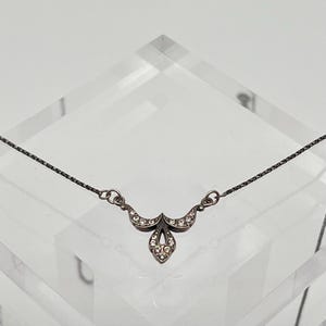 Può includere: Una collana d'argento con un delicato ciondolo che presenta un design floreale stilizzato accentuato da piccoli cristalli trasparenti.