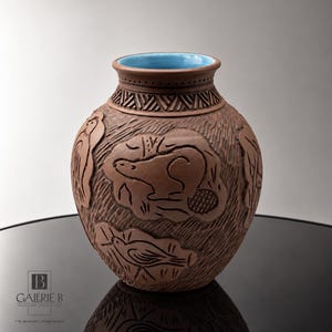 Könnte beinhalten: Eine braune Tonvase mit strukturierter Oberfläche, die Reliefschnitzereien eines Bibers und von Vögeln zeigt. Die Vase hat einen breiten, bauchigen Körper, einen schmalen Hals mit geometrischen Mustern und eine hellblaue Glasur innen.