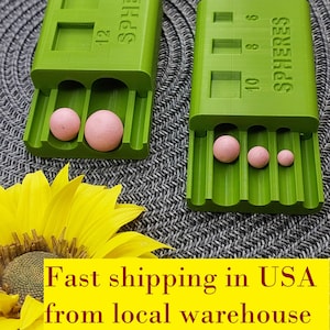 May include: Green plastic sphere size gauge with three rows of holes and a label that reads "SPHERES". The gauge is open and shows three pink spheres of different sizes.