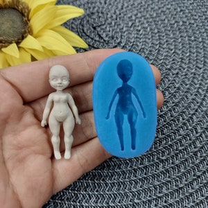 Puede incluir: Un molde de silicona blanco para hacer una pequeña figura de muñeca. El molde es azul y tiene un contorno detallado de una muñeca con brazos, piernas y cabeza. Una muñeca terminada hecha con el molde se muestra junto al molde.
