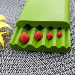 May include: A green plastic storage case with four red diamond-shaped objects of varying sizes inside. The case has a textured surface and a hinged lid.