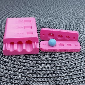May include: Pink plastic mold with three round cavities for making resin beads. The mold is open and a blue resin bead is sitting in the largest cavity. The mold has measurements labeled on the bottom: 10 mm, 8 mm, 6 mm, and 3 mm.