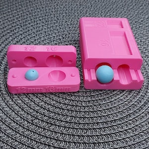 Peut inclure: Moule en plastique rose avec deux compartiments pour la fabrication de perles rondes. Le moule est marqué pour des perles de 12 mm et 16 mm. Une perle bleue est dans l'un des compartiments.