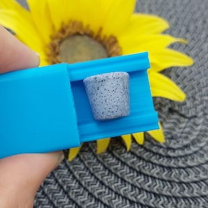 Op de afbeelding: Een blauwe siliconen mal met een klein grijs en wit glitterpotje erin.