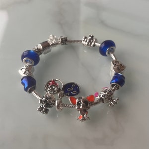 May include: A silver charm bracelet with blue and clear glass beads, a silver heart charm, a silver clock charm, a silver Mickey Mouse charm, a silver dog charm, and a silver crown charm.