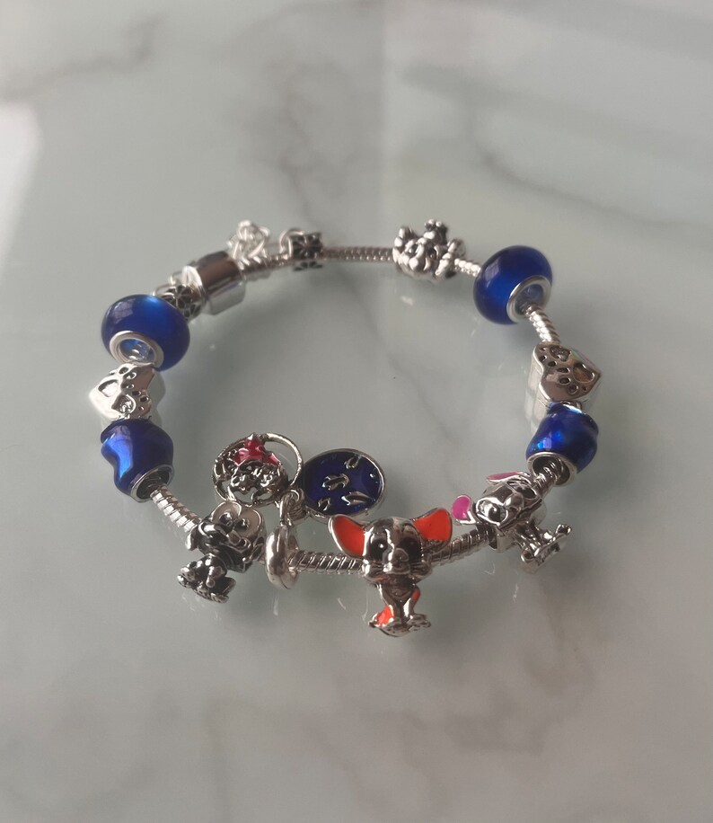 May include: A silver charm bracelet with blue and clear glass beads, a silver heart charm, a silver clock charm, a silver Mickey Mouse charm, a silver dog charm, and a silver crown charm.