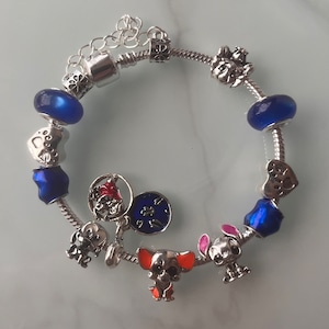 May include: A silver charm bracelet with blue and clear glass beads, silver charms of hearts, paw prints, a dog, a star, and a clock face.