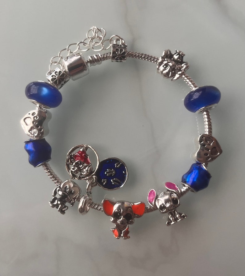 May include: A silver charm bracelet with blue and clear glass beads, silver charms of hearts, paw prints, a dog, a star, and a clock face.