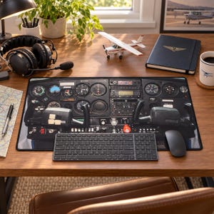 Könnte beinhalten: Eine rechteckige Schreibtischunterlage mit einem hochauflösenden Druck eines Flugzeug-Cockpit-Instrumentenbretts, einschließlich verschiedener Anzeigen, Skalen und zwei Steuerhörnern. Die Unterlage liegt auf einem Holztisch unter einer Tastatur und Maus.