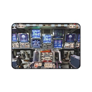 May include: A view of the cockpit of a spacecraft with multiple digital displays and control panels. The displays show various readings and data, including numbers and symbols. The panels have buttons, switches, and knobs.