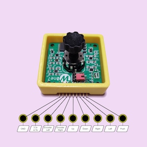 May include: A yellow plastic enclosure containing a green circuit board. The board features a rotary encoder with a black knob and a push button. The enclosure has eight pins on the bottom, labelled GND, 3.3v or 5v, Encoder Left, Encoder Right, Up, Down, Right, Left, and Push.
