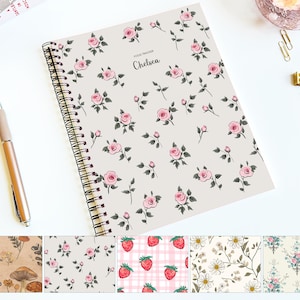 May include: A spiral-bound notebook with a floral pattern of pink roses and green leaves on a cream background. The text "FOOD TRACKER" and the name "Chelsea" are printed on the cover. A gold pen and paper clips are visible.