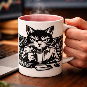 Może przedstawiać: Biały ceramiczny kubek z czarno-białą ilustracją kota trzymającego filiżankę kawy. Kubek ma różowe wnętrze i paruje. Kot znajduje się w otoczeniu biznesowym, z ekranem komputera w tle.