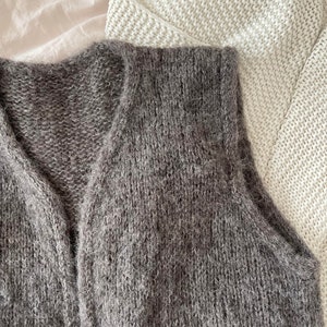 Könnte beinhalten: Eine graue, flauschige Strickweste mit V-Ausschnitt.