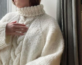 May include: A white cable knit turtleneck sweater with a loose fit.