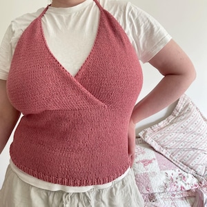 May include: A pink knitted halter top with a criss-cross front. The top is made of a soft, textured yarn and has a relaxed fit.
