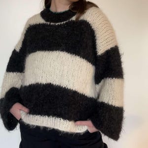 Może przedstawiać: Puszysty sweter w czarno-białe paski z okrągłym dekoltem.