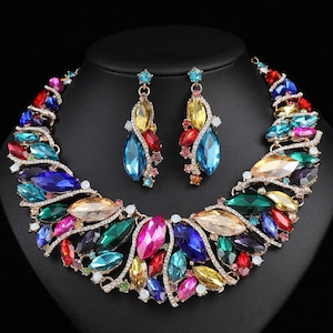 May include: A colourful necklace and earring set with a striking arrangement of gemstones. The necklace and earrings display a variety of jewel-toned stones in shades of blue, green, pink, and yellow, set in a gold-toned metal.