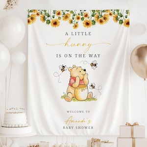 Puede incluir: Una pancarta blanca para baby shower con un borde de girasoles y el texto "A Little Hunny Is On The Way". Winnie the Pooh aparece con un tarro de miel y abejas. La pancarta dice "Welcome to Amanda's Baby Shower."