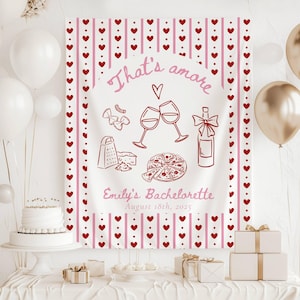 May include: A white bachelorette party banner with pink and red hearts and stripes. The banner says "That's amore" and "Emily's Bachelorette August 18th, 2025". There are illustrations of wine glasses, a bottle of wine, a pizza, and pasta.
