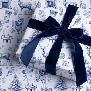 Puede incluir: Una caja de regalo rectangular envuelta en papel blanco con un patr&oacute;n navide&ntilde;o azul repetitivo de estilo toile que muestra ciervos, Pap&aacute; Noel, p&aacute;jaros, calcetines y &aacute;rboles, atada con un lazo grande de cinta de terciopelo azul marino oscuro.