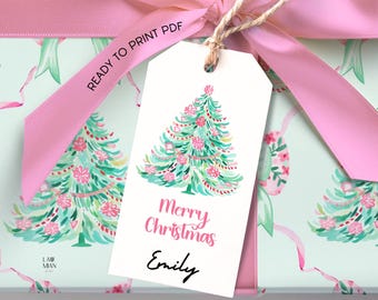 Puede incluir: Una etiqueta de regalo con un diseño de árbol de Navidad en acuarela, con tonos rosas y verdes. La etiqueta dice "Merry Christmas Emily" y está atada con hilo a un regalo envuelto con una cinta rosa. El papel de regalo tiene un patrón repetido de árbol de Navidad.