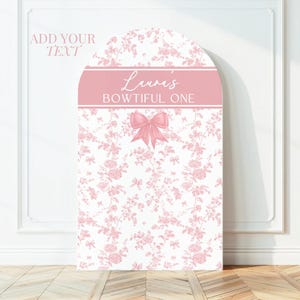 May include: A pink and white floral design arch-shaped sign with the text "Luvvi's BOWTIFUL ONE" in a pink banner. A pink bow is centered below the banner. The words "ADD YOUR TEXT" are in the upper left corner.