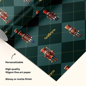 May include: Wrapping paper featuring a dark green and black argyle pattern with thin gold grid lines. The design includes repeating illustrations of red and gold nutcracker figures and the name Andrew printed in gold script lettering.