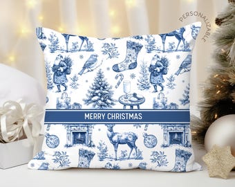 Puede incluir: Un cojín cuadrado con un patrón navideño azul y blanco estilo toile, con ilustraciones de Santa Claus, ciervos, pájaros, calcetines y árboles. Una banda azul horizontal en el centro muestra el texto MERRY CHRISTMAS.